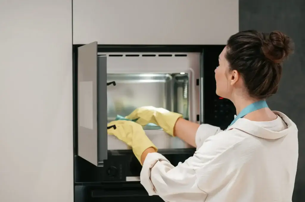 A woman in yellow gloves cleaning the microwave