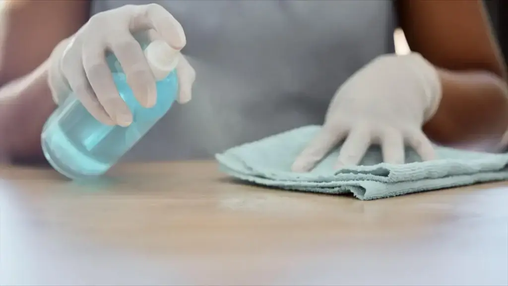 hands spraying and wiping wooden table with cloth