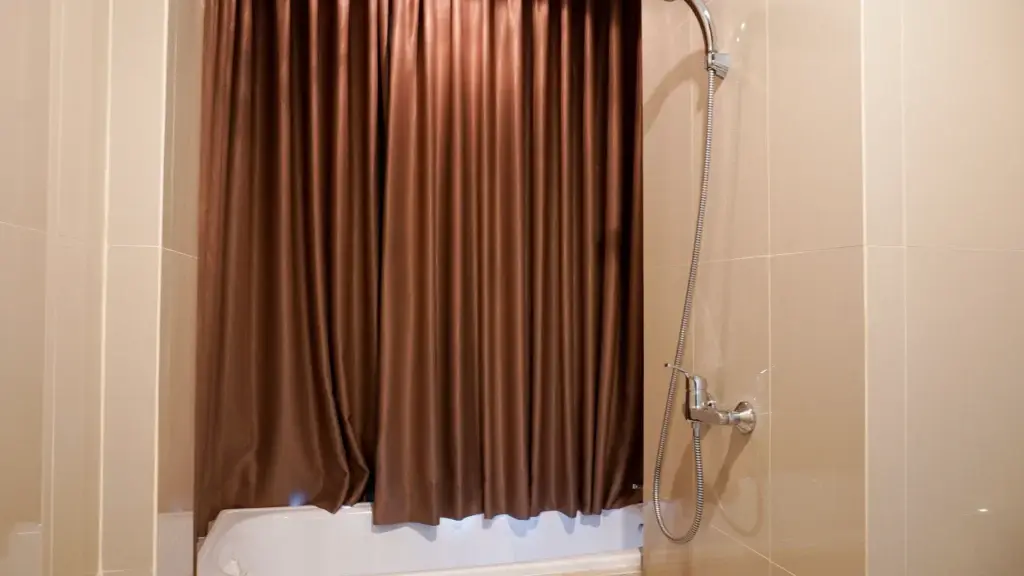 Bathtub with brown curtain and silver showerhead on beige tiled wall