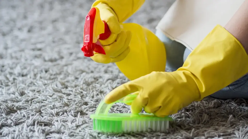Hands with yellow gloves spraying and scrubbing gray carpet