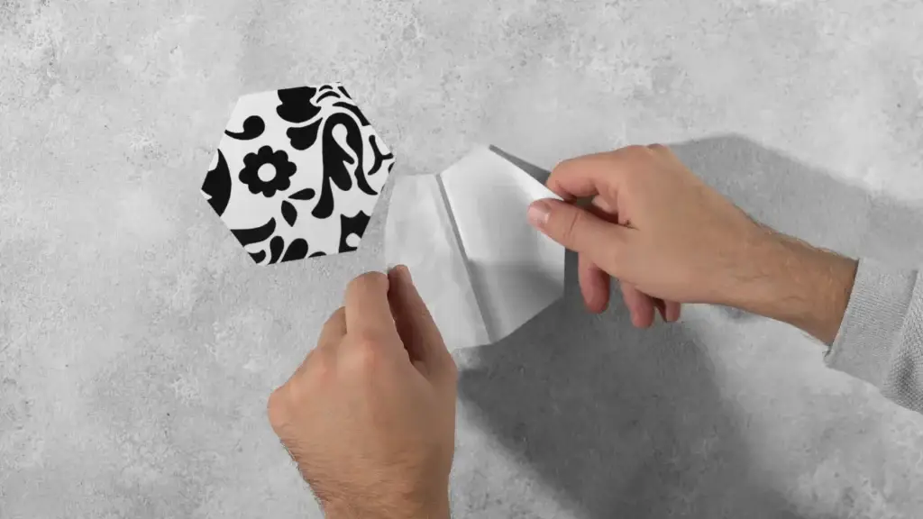Hands peeling backing off decorative vinyl tile